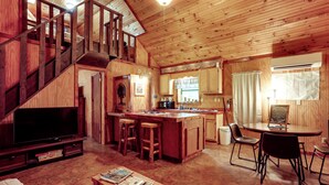 Ein Holz-Blockhaus mit Fernseher, Barhocker, Esstisch und Küchenzeile.