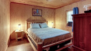 A wooden room with a bed, a nightstand, a wall-mounted shelf, and a window with curtains.