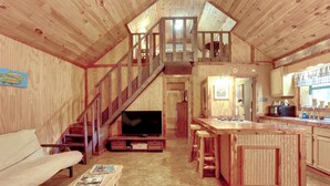 A wooden interior with a sofa, TV, kitchen, and a staircase.