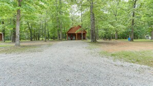 A cabin in a forest with a gravel driveway and a picnic table.