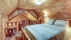Ein Holzhäuschen im Inneren mit einem Bett, einem kleinen Tisch und einer Treppe.