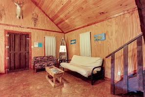 A wooden interior with a sofa, a patterned chair, a wooden table, and a door. - Near Blanchard Springs! Classic Cabin in the Woods (Fifty-Six)