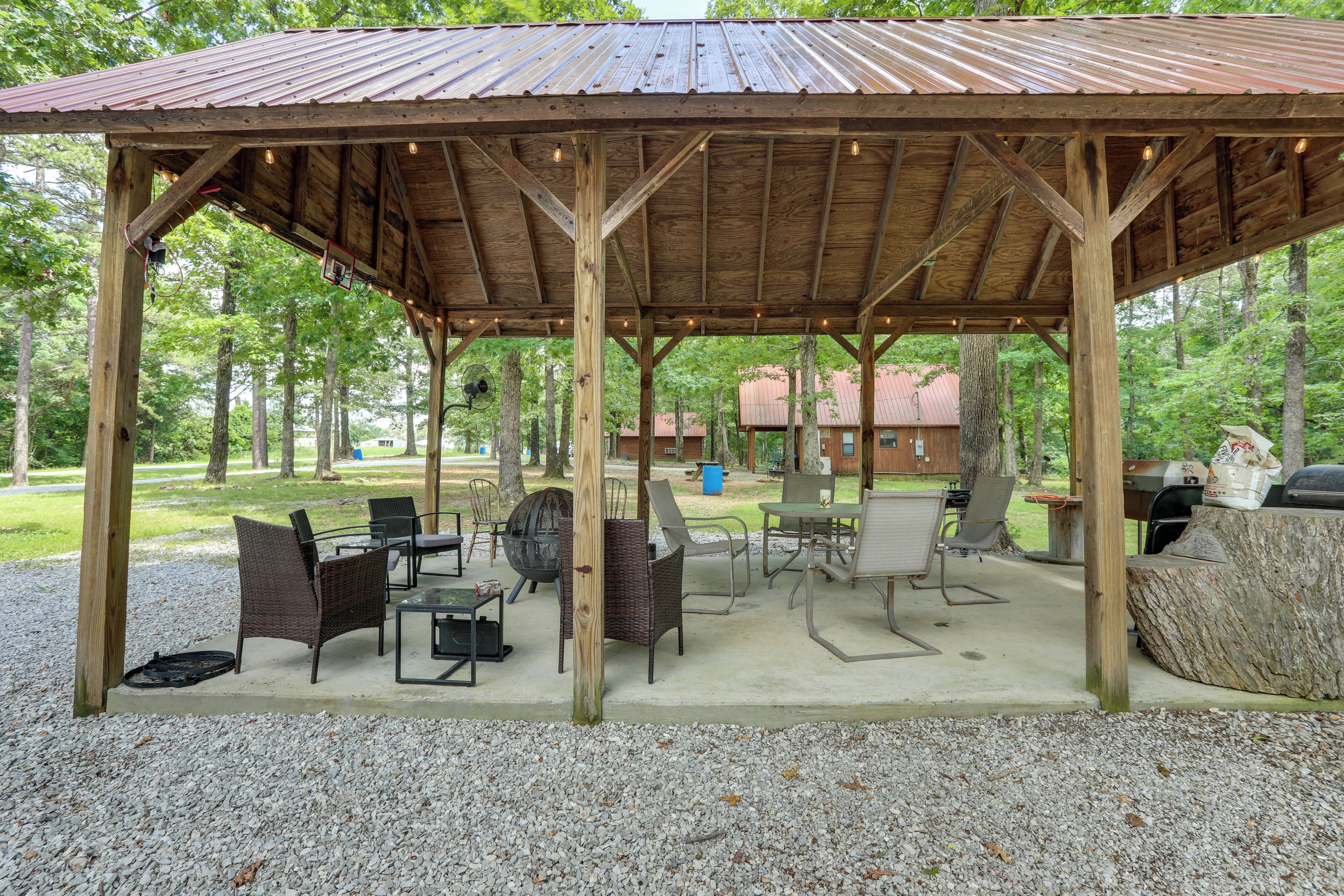 A covered outdoor seating area with tables and chairs, surrounded by trees.