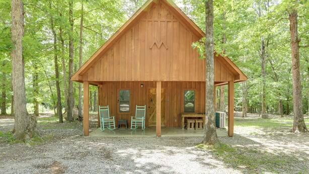 A wooden cabin with a porch, two rocking chairs, and a table.
