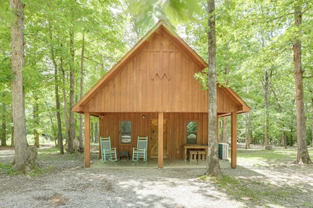 A wooden cabin with a porch, two rocking chairs, and a table.