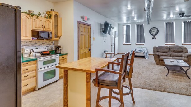 Cocina con armarios de madera, microondas y estufa. Se aprecia una mesa de comedor con sillas.