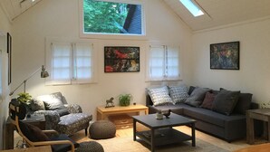 A spacious loft with high ceilings, a large skylight, a cozy seating area with a sofa and armchairs, and a wooden coffee table.
