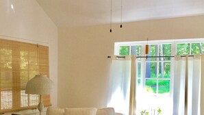 A room with a wooden floor, a sofa, a table, a lamp, a radiator, and a window with curtains.