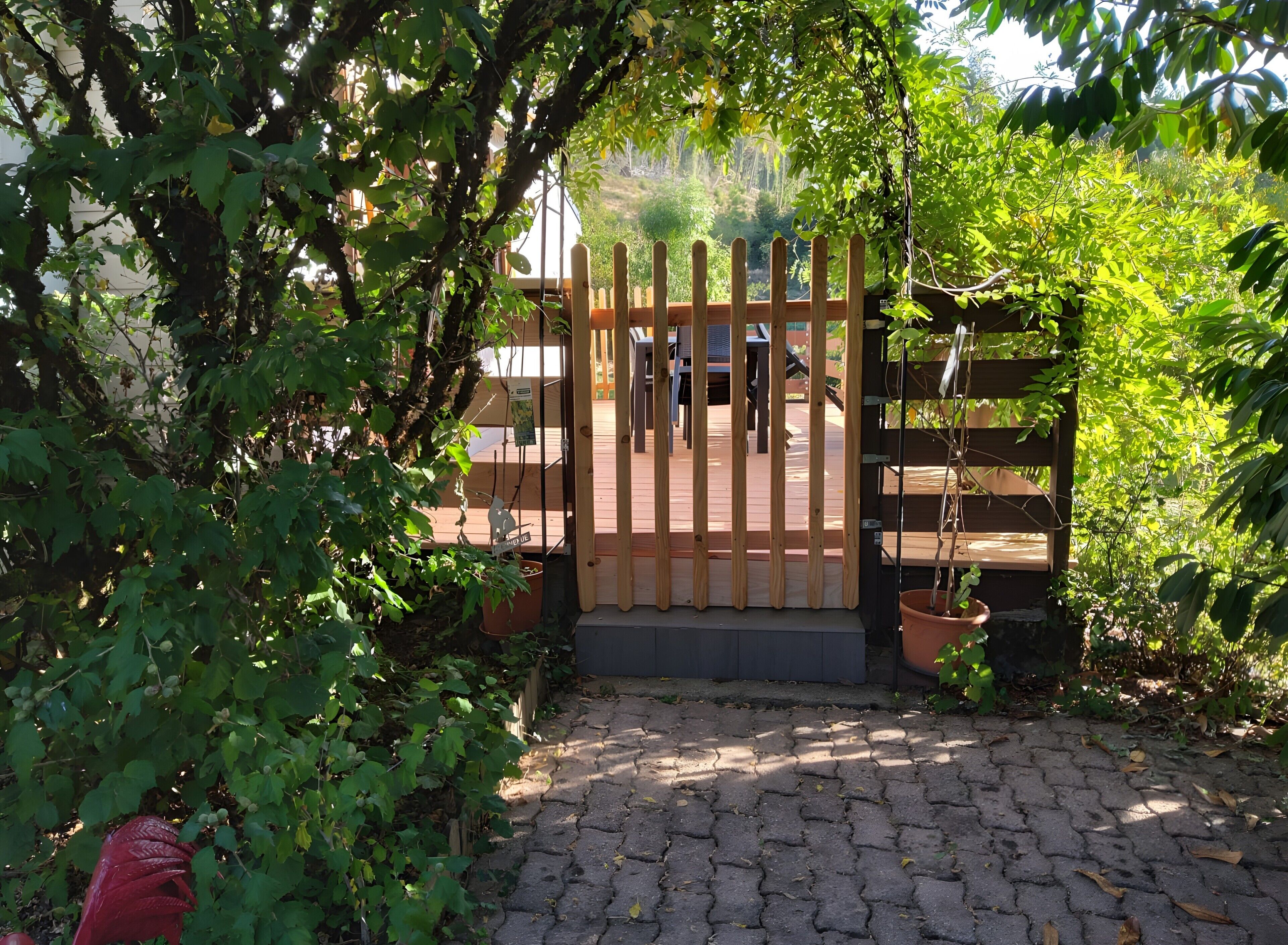 A wooden gate with a sign, a paved pathway, and lush greenery.