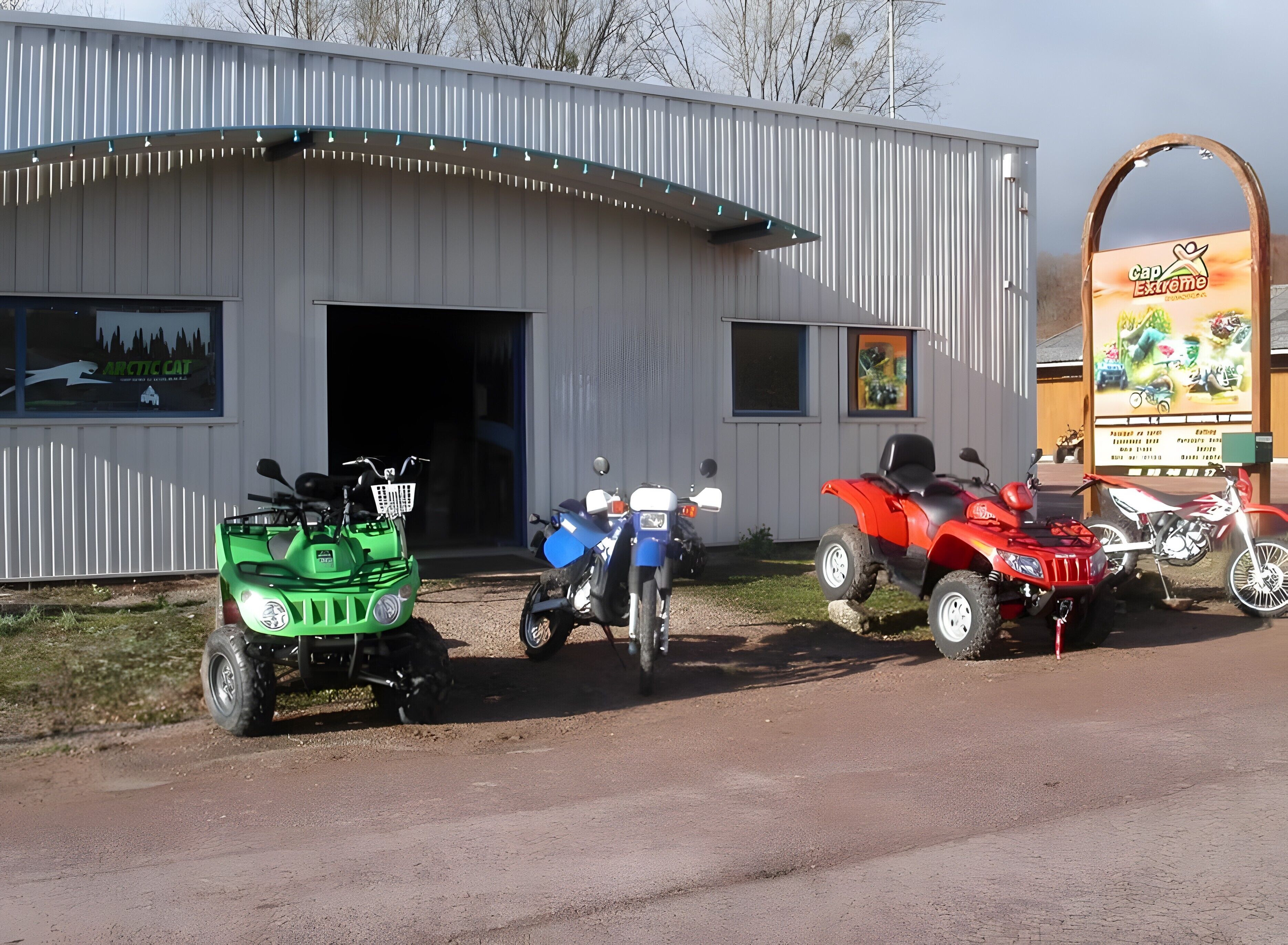 A building with a garage door, a signboard, and three ATVs parked in front.