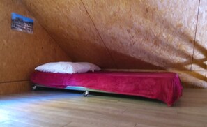 Ein kleines Zimmer mit einem Einzelbett, Holzbalkendecke und einem sichtbaren Poster an der Wand.