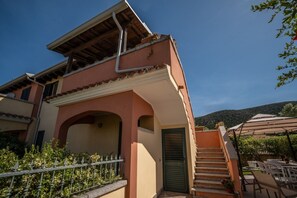 Ein zweistöckiges Gebäude mit Balkon, Treppe und Außenbestuhlung.