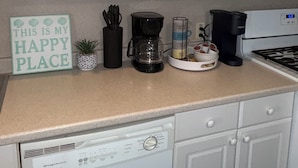 A kitchen with white cabinets, a coffee maker, a coffee pot, a sign saying 'THIS IS MY HAPPY PLACE,' and a dishwasher. - Renovated Beach Condo, 1 Block to the Beach (Wildwood)