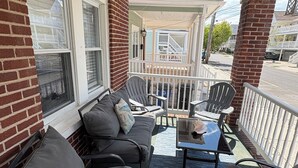 A covered porch with a seating area, including a sofa and chairs, and a small table. - Renovated Beach Condo, 1 Block to the Beach (Wildwood)