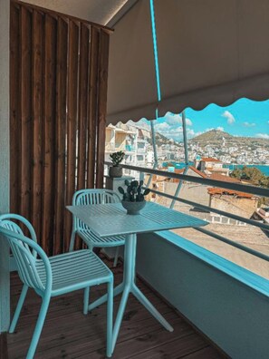 A balcony with a table and chairs, a potted plant, and a view of a coastal cityscape. - SIÁMAR Studio Rooms (Saranda)