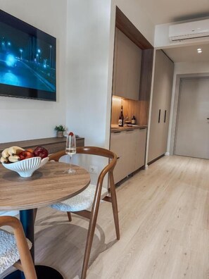 A modern kitchen with wooden cabinets, a dining table with chairs, a bowl of fruit, and a wine glass. - SIÁMAR Studio Rooms (Saranda)