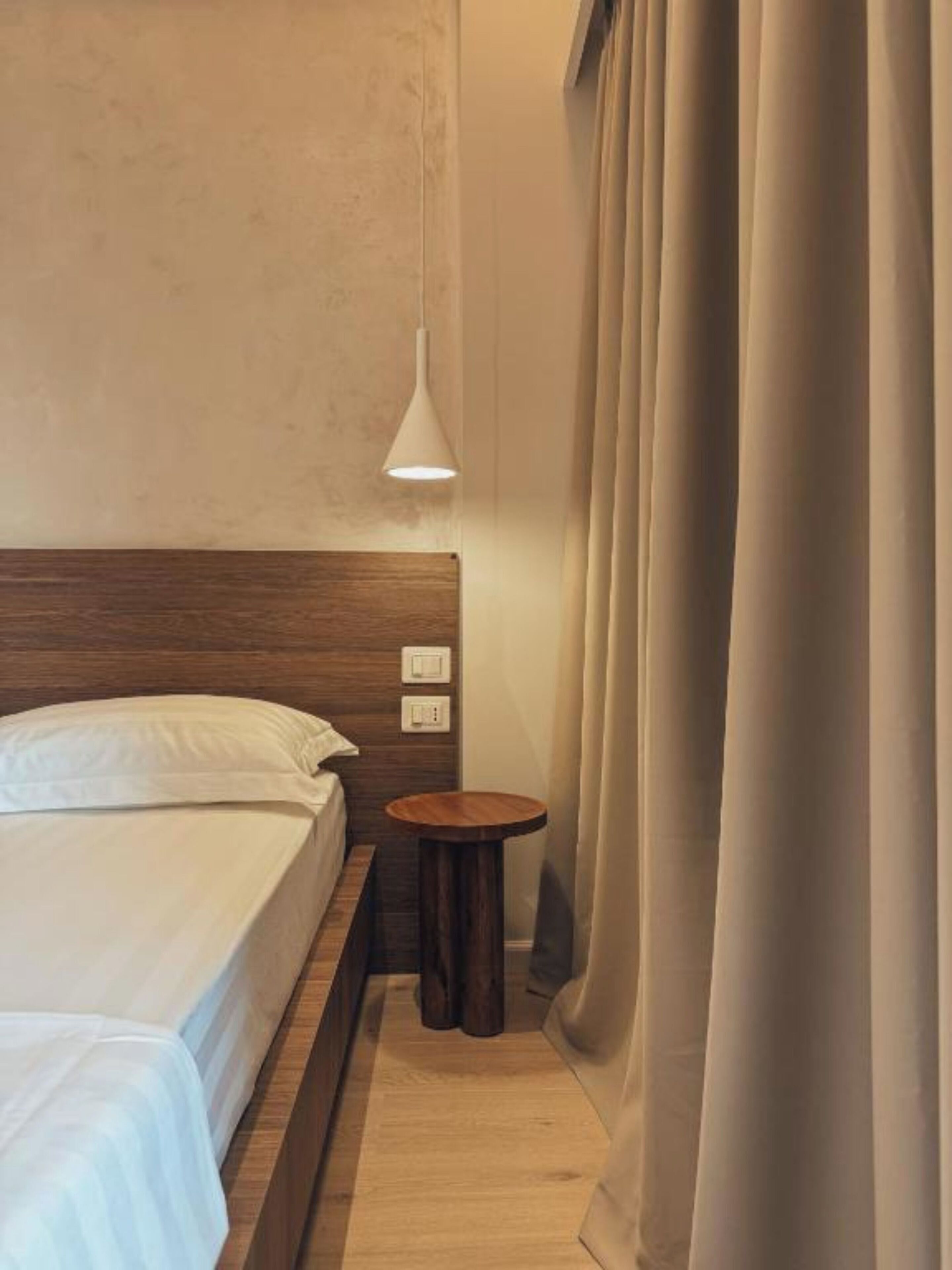 Een hotelkamer met een houten hoofdeinde, een nachtkastje, een lamp en een gordijn.