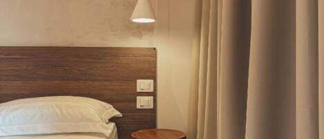Een hotelkamer met een houten hoofdeinde, een nachtkastje, een lamp en een gordijn.