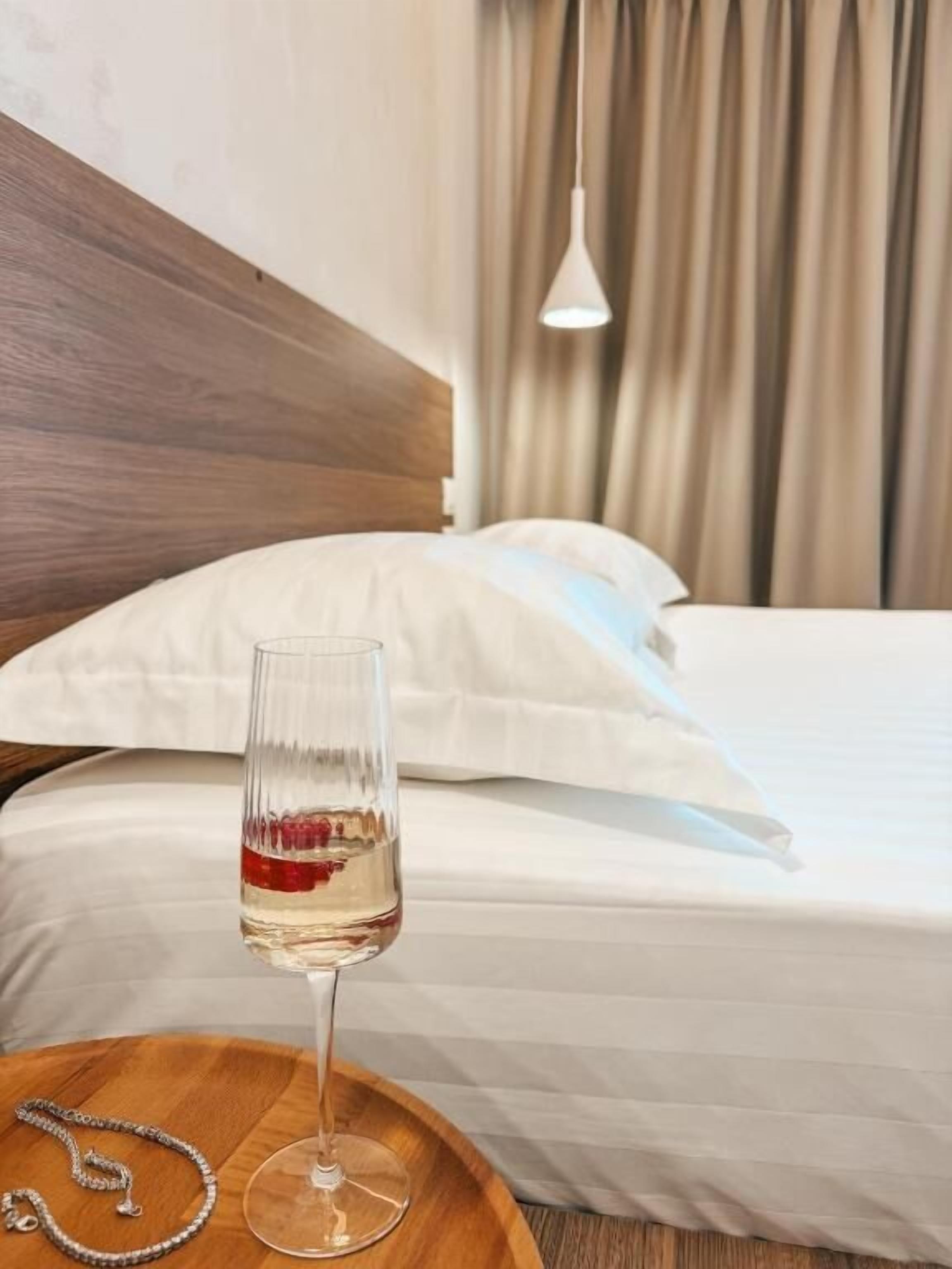 A hotel room with a wooden headboard, a bed with white bedding, a bedside table with a glass of water, and a hanging light fixture.