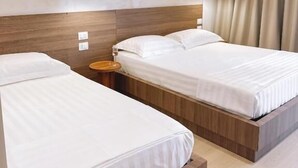Ein Hotelzimmer mit zwei Betten, einem Holzkopfende, einem Nachttisch und einem großen Fenster mit Vorhängen.