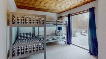 A room with bunk beds, a window with curtains, and a view of the outside.