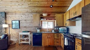 A wooden cabin interior with a kitchen featuring a stove, microwave, and wooden cabinets. - Meadow's Edge at Black Butte Ranch—2 pets allowed (Sisters)