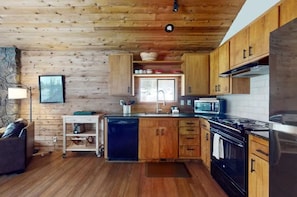 A wooden cabin interior with a kitchen featuring a stove, microwave, and wooden cabinets. - Meadow's Edge at Black Butte Ranch—2 pets allowed (Sisters)