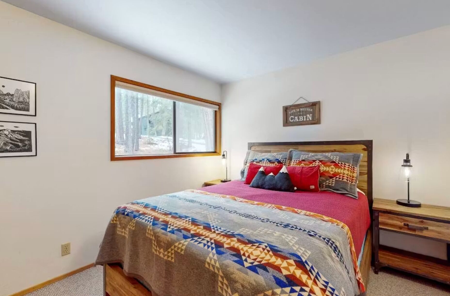 A bedroom with a bed, a nightstand, a window, and a wall sign.