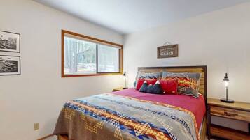 A bedroom with a bed, a nightstand, a window, and a wall sign.