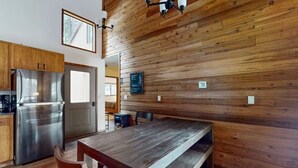 A kitchen with wooden paneling, a stainless steel refrigerator, a wooden dining table, and a bench. - Meadow's Edge at Black Butte Ranch—2 pets allowed (Sisters)