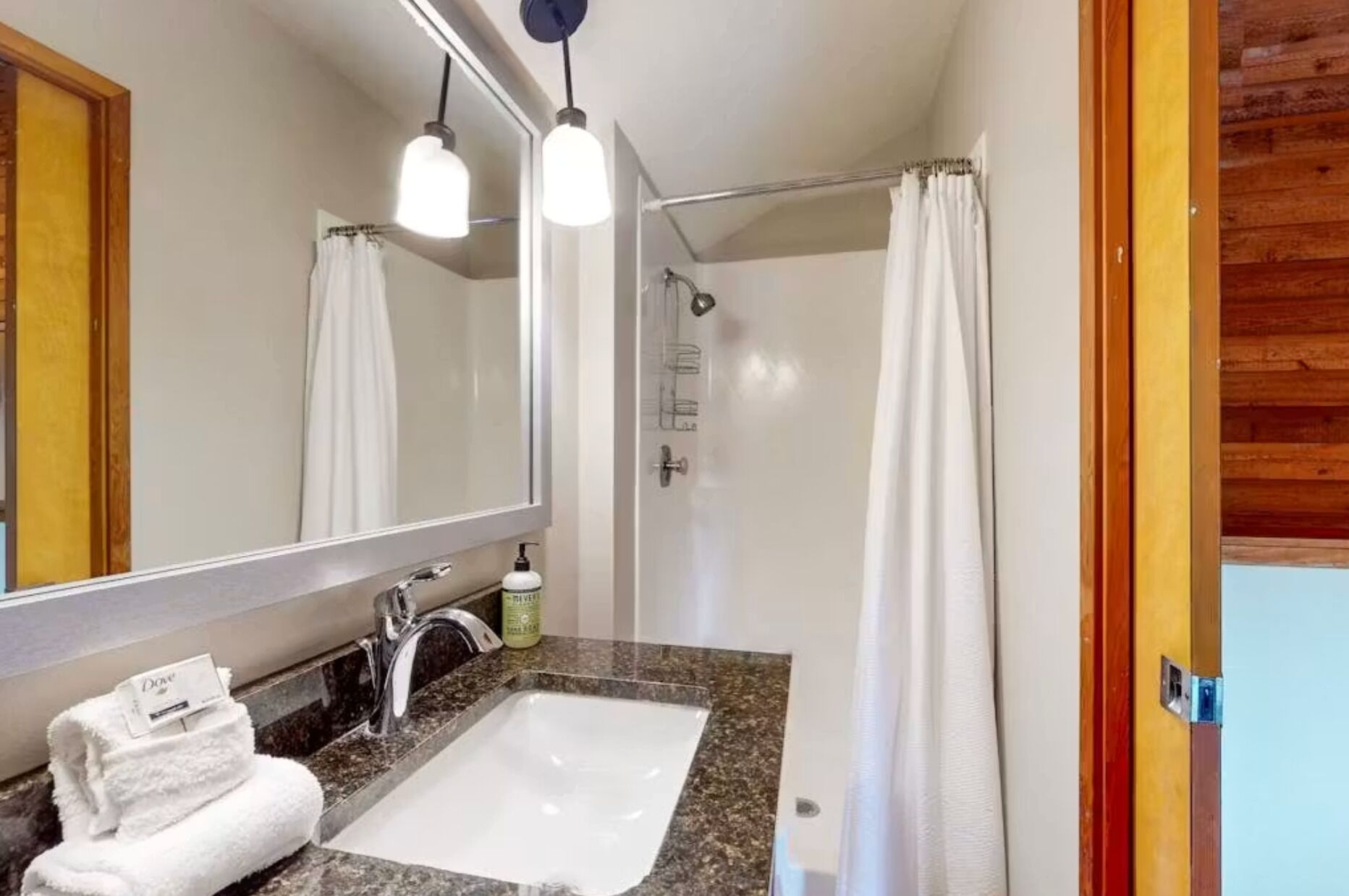 Un baño con lavamanos, espejo, ducha y toallero.