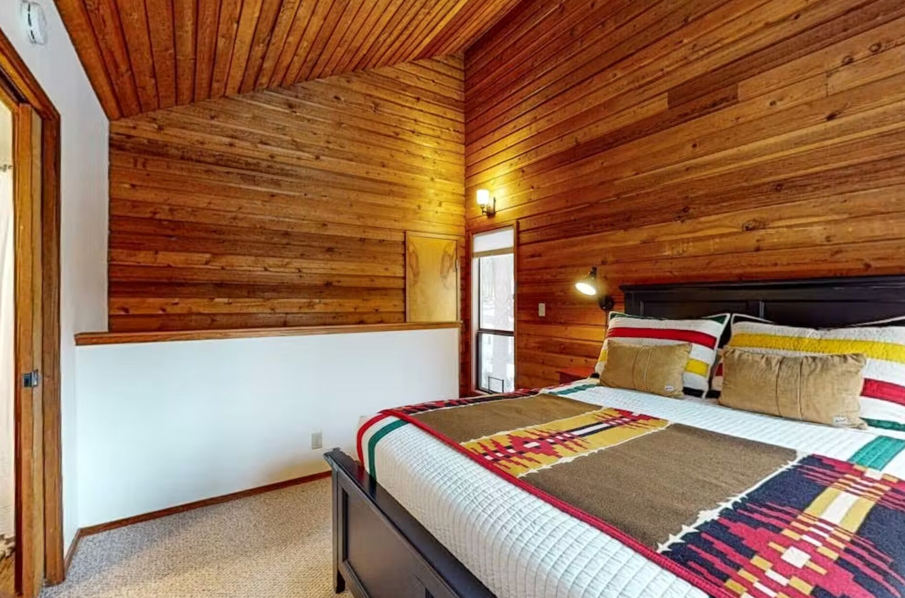 A wooden-paneled room with a bed, a window, and a door.