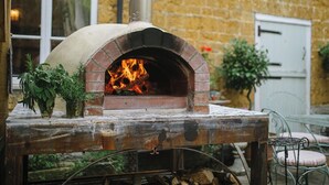 En pizzaugn av tegelsten, med en brasa som brinner inuti, placerad på ett rustikt bord med ett fönster i bakgrunden.