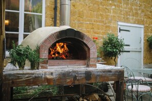 A brick oven pizza oven with a fire burning inside, placed on a rustic table with a window in the background.