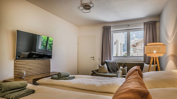 A hotel room with a bed, a TV, a lamp, and a window with curtains. - Sophi's Wiesenglück (Dorfgastein)