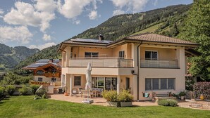 A two-story building with a balcony, solar panels, and a well-maintained lawn. - Sophi's Wiesenglück (Dorfgastein)