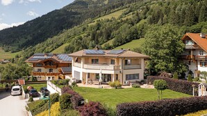 A modern two-story house with solar panels, a well-maintained lawn, and a mountainous backdrop. - Sophi's Wiesenglück (Dorfgastein)