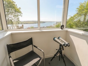 Una habitación con un ventanal grande con vistas a una masa de agua, un telescopio sobre un trípode y una silla plegable.