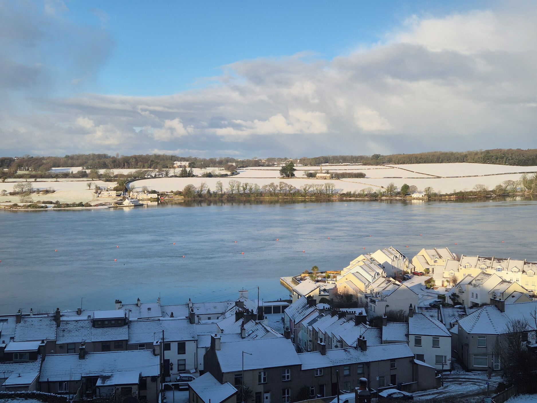 A residential area with snow-covered rooftops and a river in the background.
