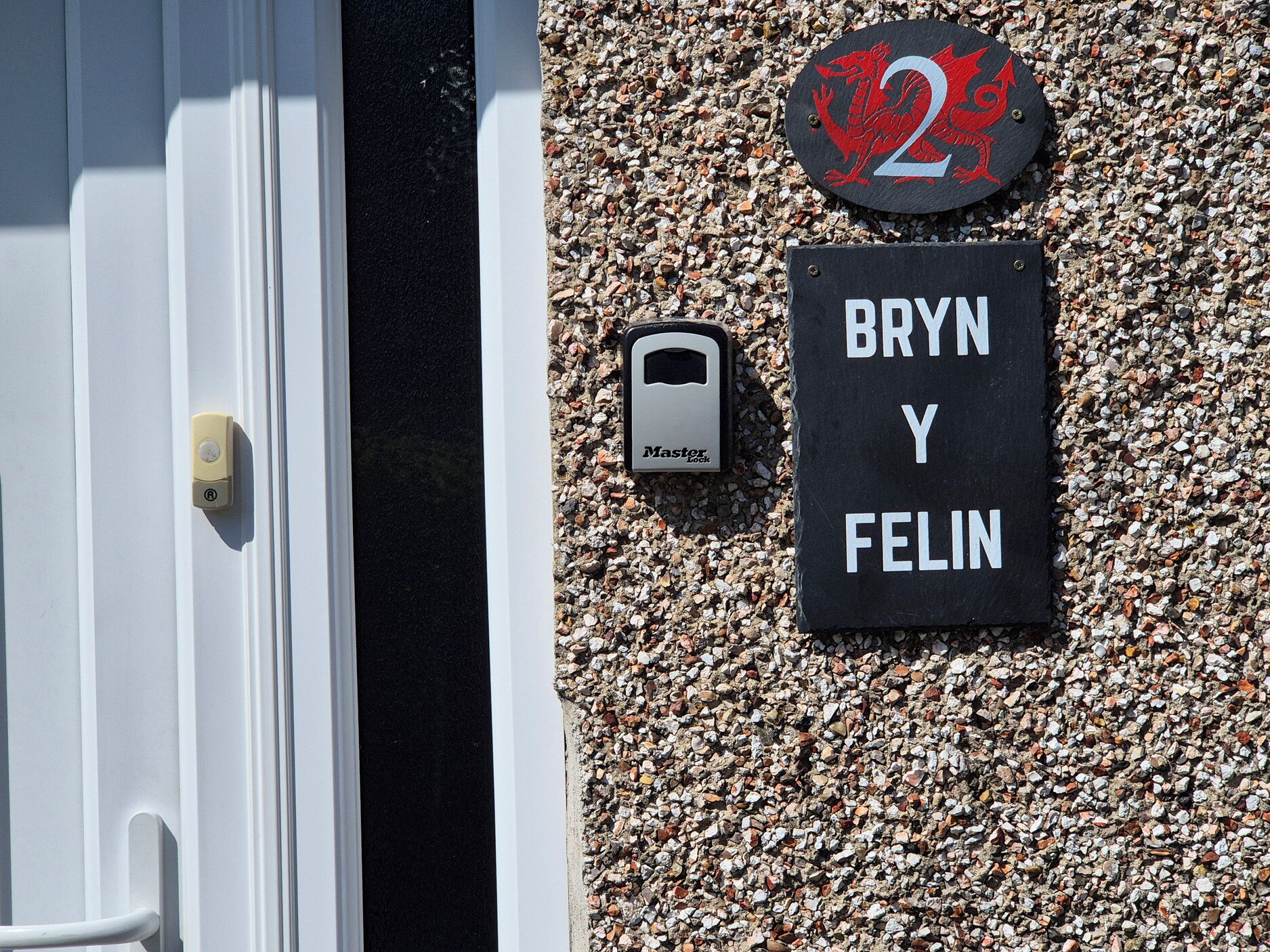 Una puerta con cerradura y llave, un letrero con el número de la casa que muestra un dragón rojo, y una placa negra con el texto 'BRYN Y FELIN'.
