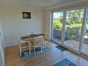 A dining area with a table and chairs, a picture on the wall, and a sliding glass door leading to an outdoor deck. - Bryn Y Felin (Y Felinheli)