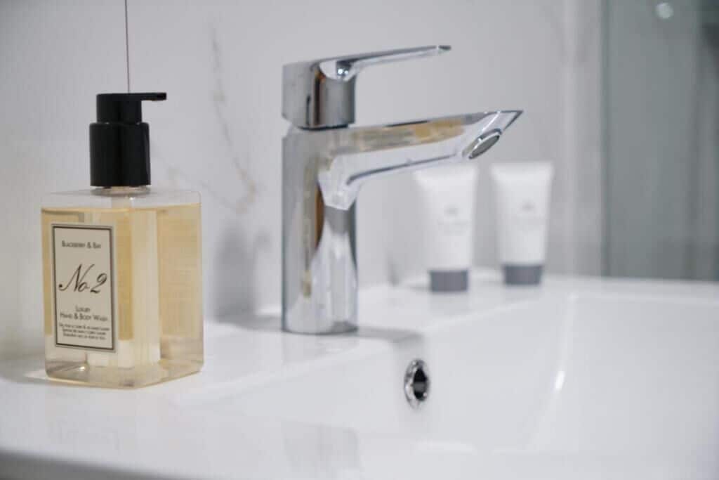 A bathroom sink with a clear bottle of liquid soap and a chrome faucet.