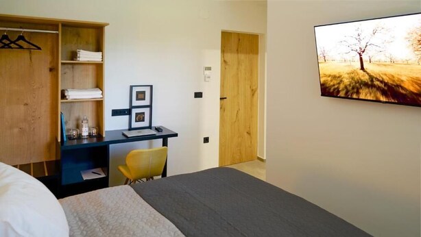 A hotel room with a bed, a desk, a chair, a wardrobe, and a painting on the wall.