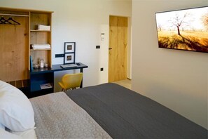 Een hotelkamer met een bed, een bureau, een stoel, een kledingkast en een schilderij aan de muur.