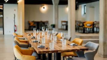 A long wooden table with chairs, set for a meal, in a modern interior with exposed beams and columns.