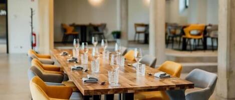 A long wooden table with chairs, set for a meal, in a modern interior with exposed beams and columns.