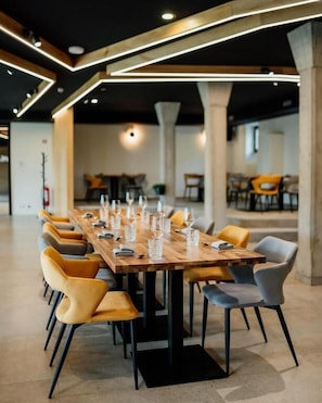 A long wooden table with chairs, set for a meal, in a modern interior with exposed beams and columns. - Posestvo Gjerkeš (Rogasovci)