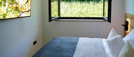 A bedroom with a bed, a window with a view of greenery, and a wall-mounted artwork.