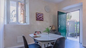A dining area with a table, chairs, a vase with flowers, a painting, and a view through a door.