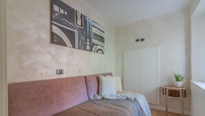 Un dormitorio con cama, una obra de arte en la pared, una mesita con una planta y un armario blanco.